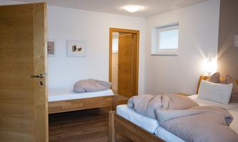 A simple and bright bedroom with two beds. The walls are kept neutral and there are wooden details.