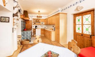 A cozy kitchen with wooden furniture and a large table. Decorative items hang on the wall and the floor is made of wood.