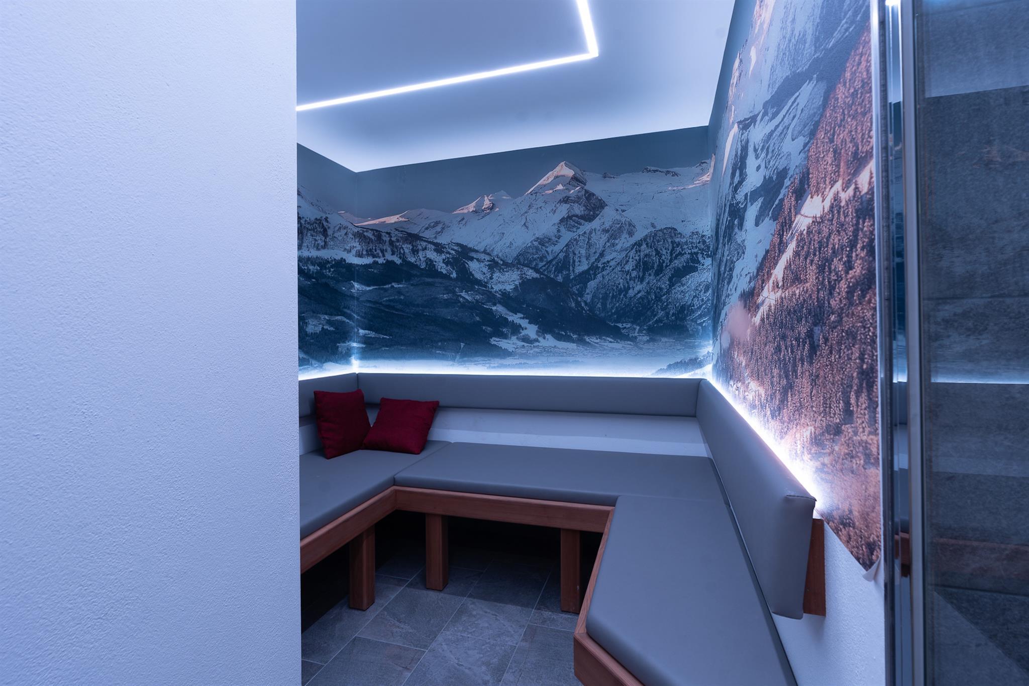A modern spa with a cozy seating area and an impressive mountain backdrop on the wall. Soft light and neutral colors create a relaxing atmosphere.