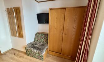 A simple room with a television and a wardrobe. In the corner, there is a cozy chair.