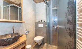 A modern bathroom with a spacious shower and an elegant stone sink. The walls are in neutral colors and there is a wooden ceiling.