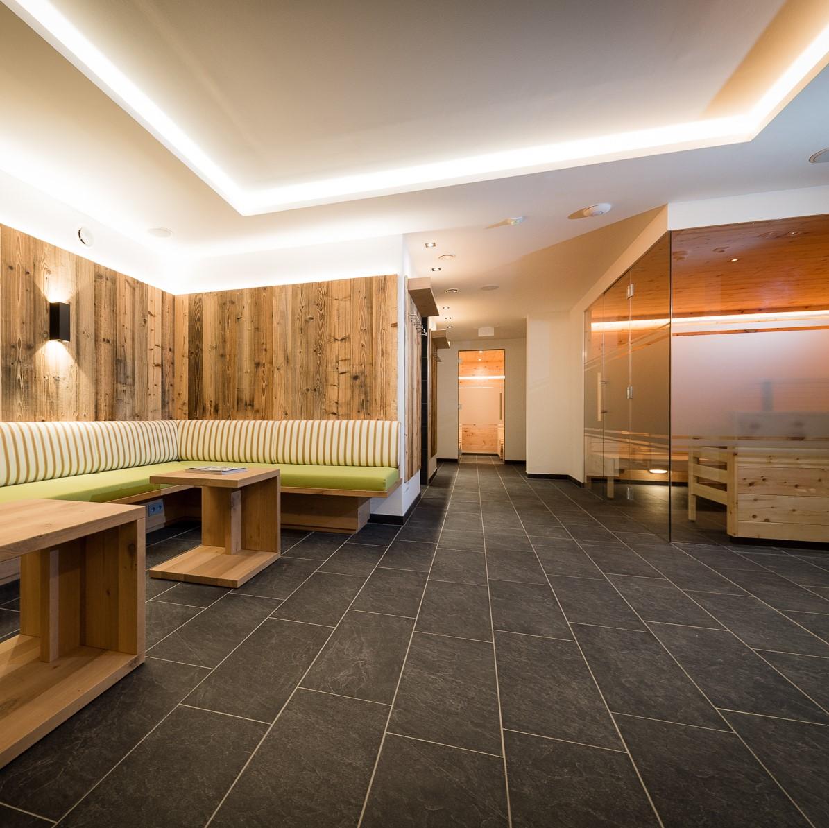 A modern relaxation room with wooden walls and a cozy seating area. The room has stylish lighting and access to a sauna.