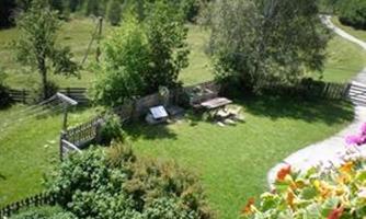 A beautiful, green garden with trees and a wooden seating area. In the background, you can see a meadow and a path.