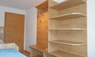 A modern room with a wooden shelf and a light wall. On the left, a door is visible that leads into the room.