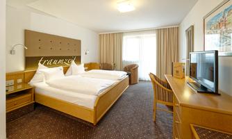 A modern hotel room with two beds, a television, and a window with curtains. The decor is simple and friendly.