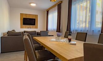 A modern dining room with a large wooden table and comfortable chairs. The windows are covered with curtains and there is a cozy feel-good atmosphere.