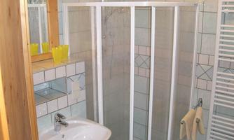 A modern bathroom with a shower enclosure and a sink. The walls are tiled, and a wooden frame complements the design.