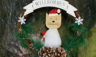 A welcome wreath with a cute cat in a Santa hat. The wreath is decorated with snowflakes and pine cones.