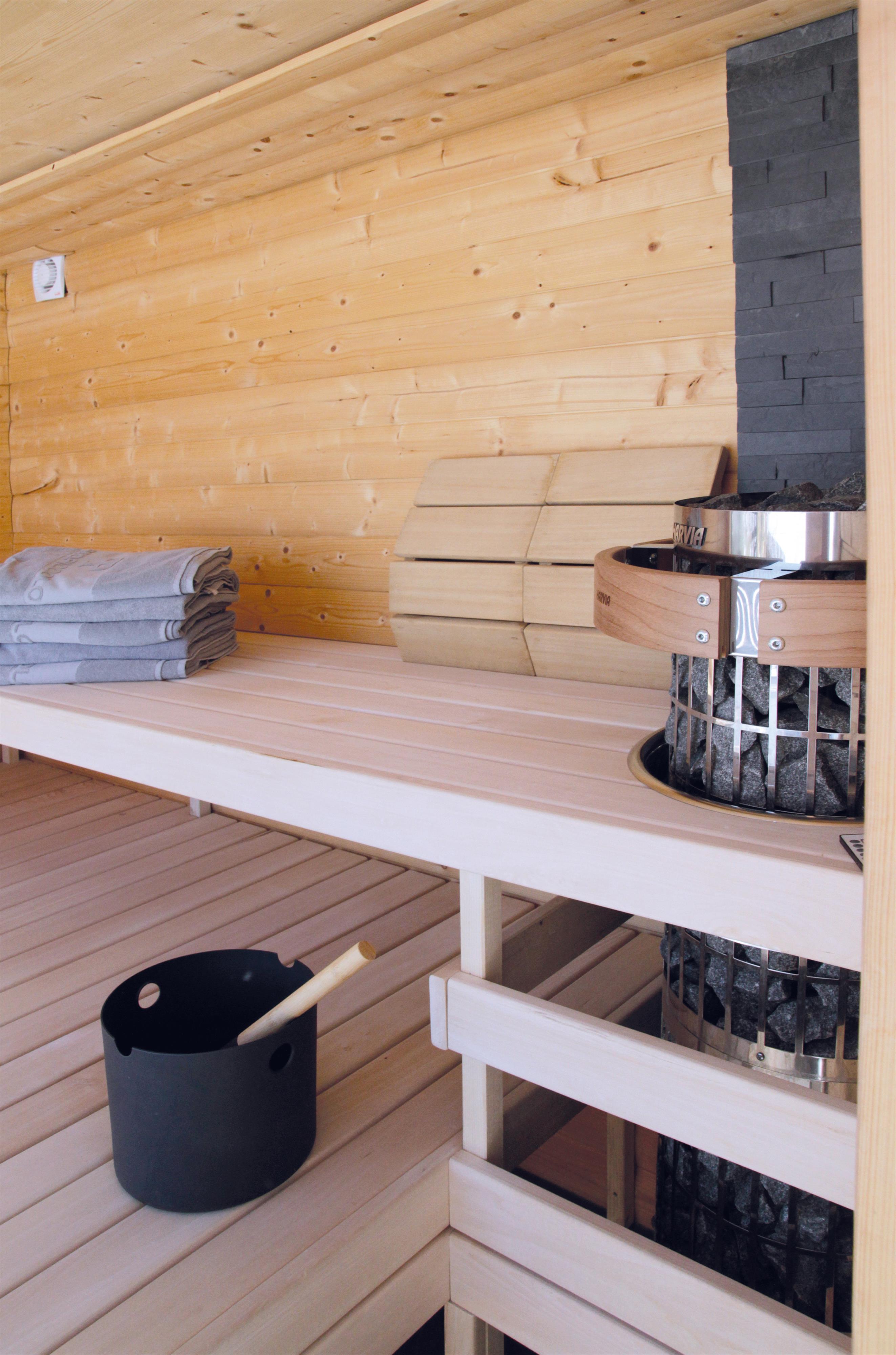 A modern sauna with wooden paneling and a stone oven. Fresh towels are ready on the benches.