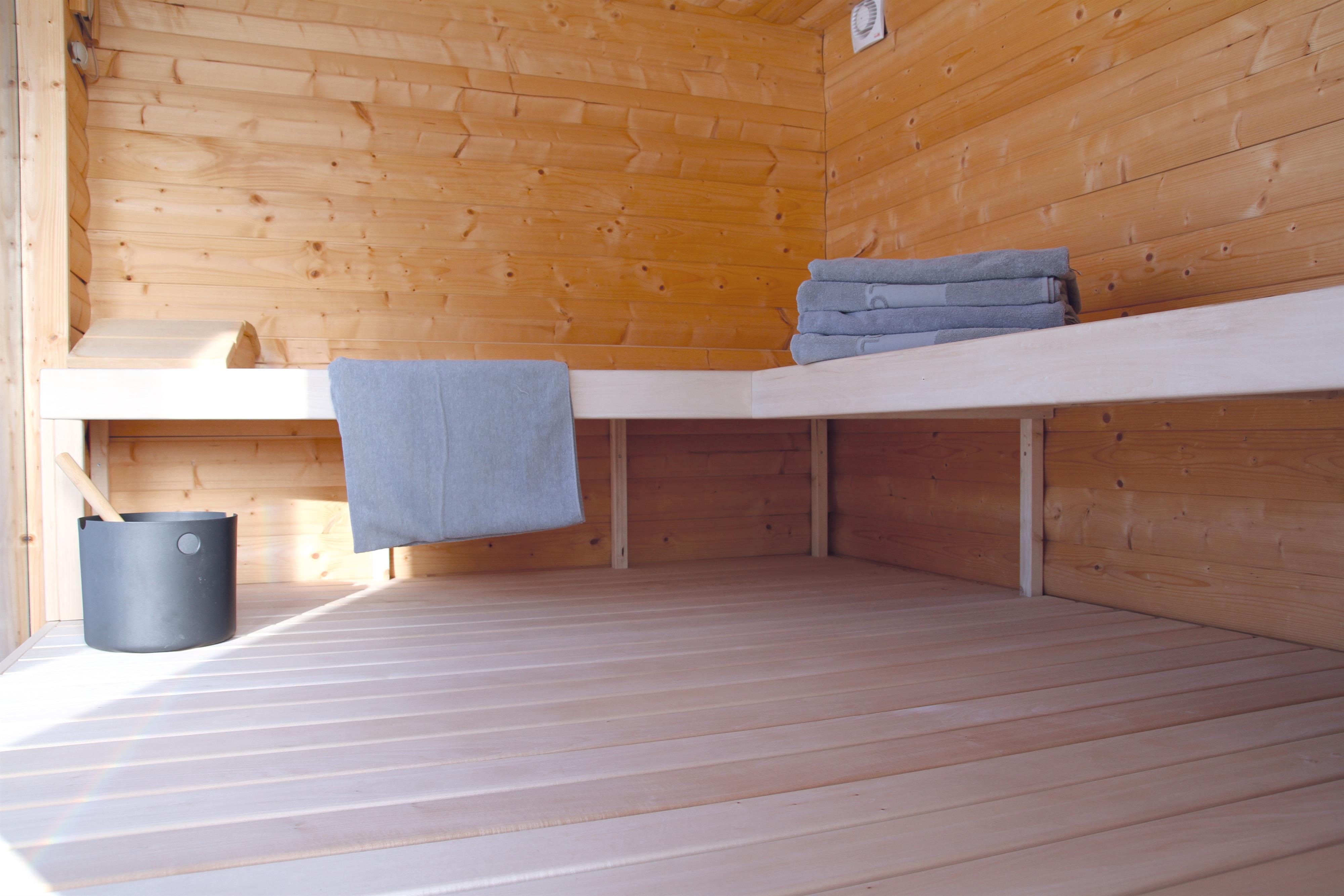 A bright sauna room made of wood with a bench and fresh towels. A bucket is ready to provide the optimal sauna experience.