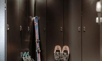 A modern ski room with black lockers and winter sports equipment. Two pairs of snowshoes and one pair of skis are visible.