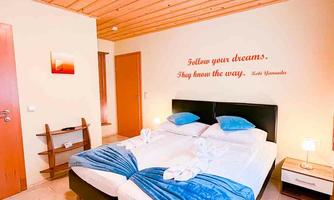 A cozy bedroom with a double bed and blue cushions. On the wall is the inspiring quote: "Follow your dreams."
