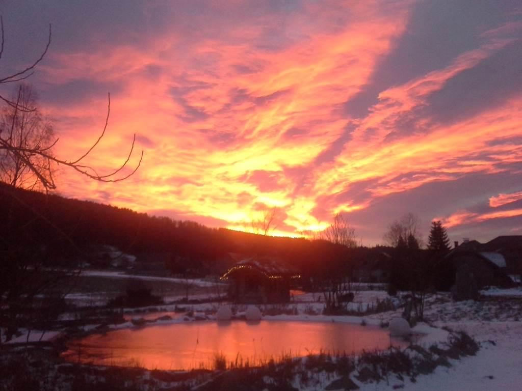 A colorful sunset over a snowy landscape. The sky glows in shades of orange and pink, while the colors are reflected in the calm water.