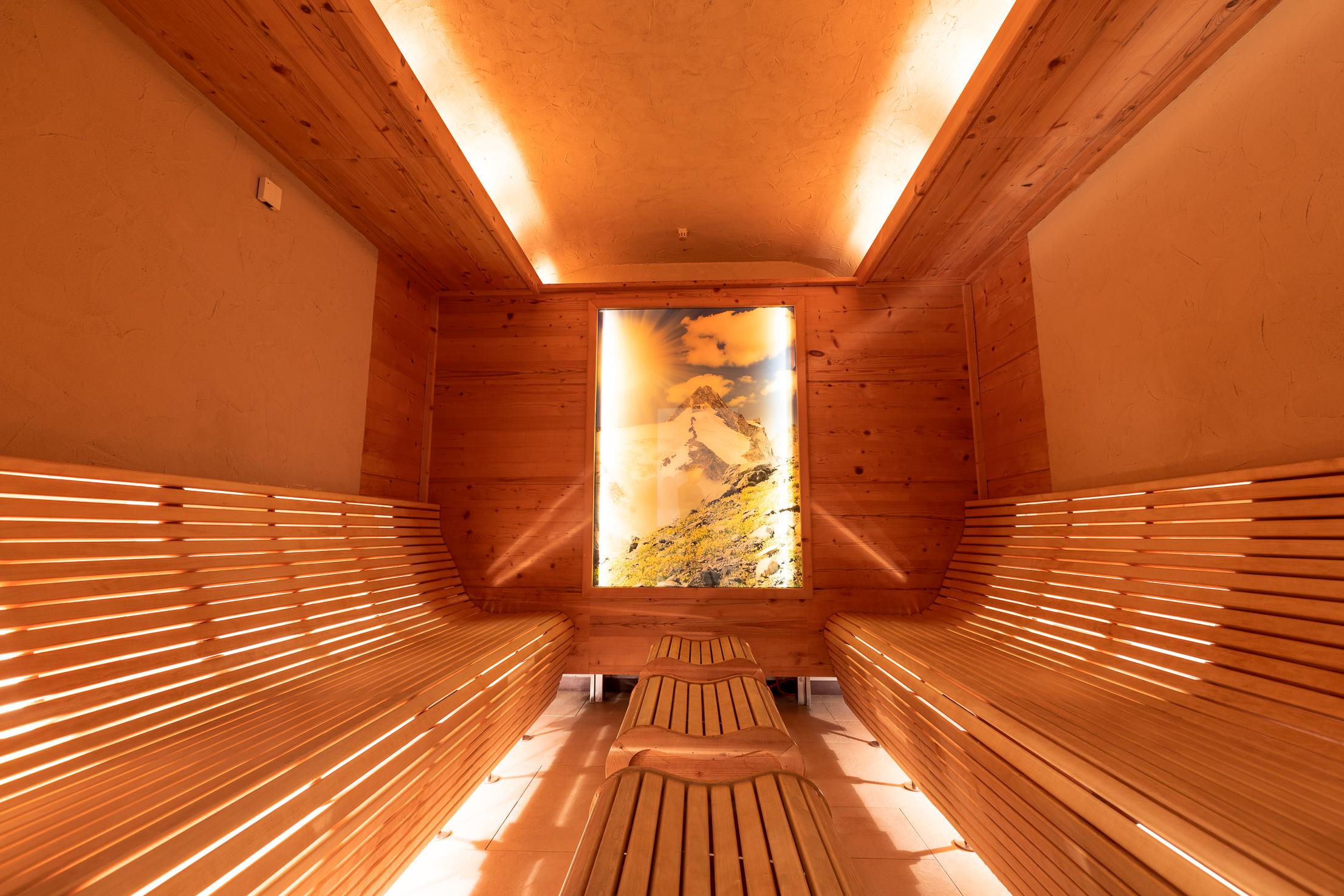 A sauna-friendly wooden cladding with benches invites you to relax. A large window reveals a tranquil mountain landscape.