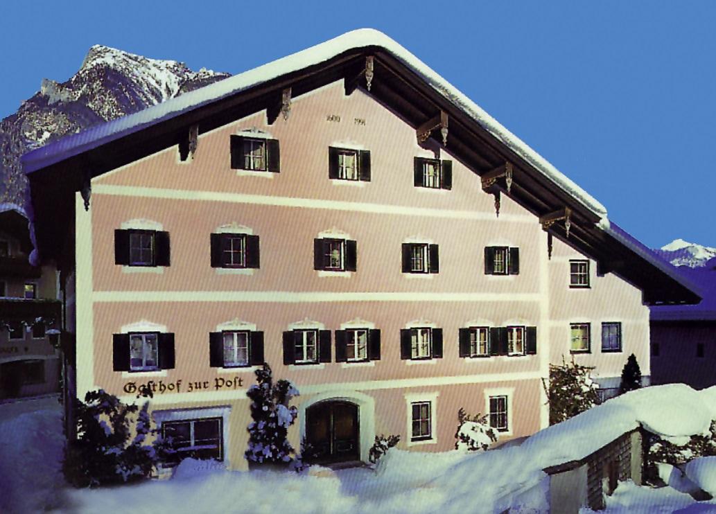 A cozy, pink inn in a snow-covered landscape. In the background, majestic mountains can be seen under a clear blue sky.