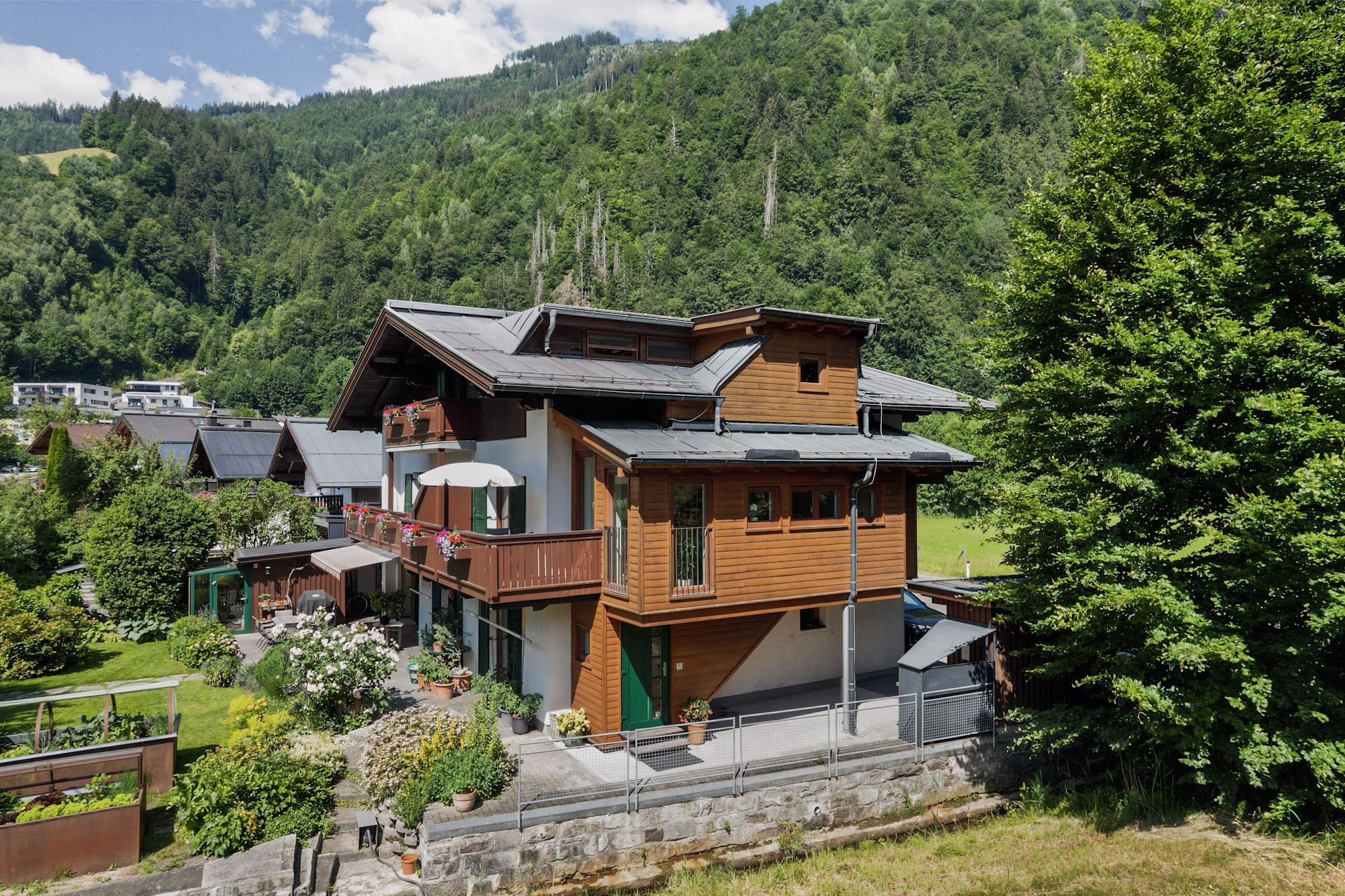 A charming wooden house with a balcony, surrounded by green hills and trees. The architecture harmonizes well with the natural surroundings.