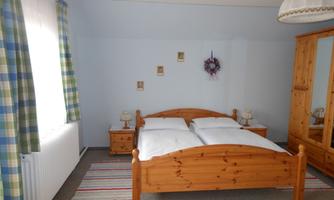 A cozy bedroom with a wooden double bed. The walls are painted light blue and there are curtains with a checked pattern.