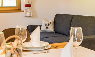 A cozy living space with a gray sofa and a cushion featuring a deer antler motif. The table is elegantly set with glasses and dinnerware.