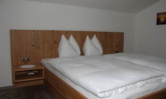 A cozy bedroom with a double bed and pillows shaped like arcs. The walls are painted in neutral colors and there is modern wooden furniture.