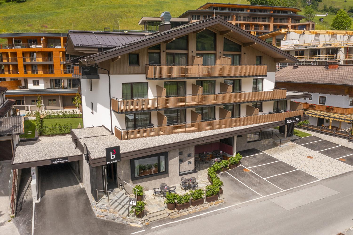 A modern building with several floors and balconies. It is located on a street and is surrounded by green meadows and other buildings.