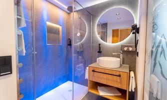 A modern bathroom with a glass shower and elegant blue lights. There is a sink on a wooden vanity and a large round mirror.