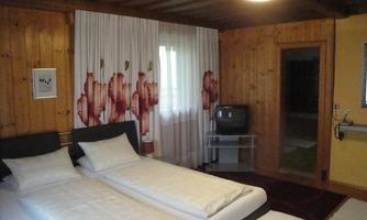 A cozy room with two single beds and wooden walls. Curtains with a floral pattern and a television complement the furnishings.