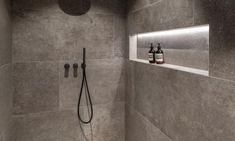 A modern shower with gray tiles and minimalist design. In the niche are two bottles of care products.