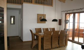 A modern dining area with a large wooden table and chairs made of rattan. Large windows provide a view outside and ensure plenty of natural light.