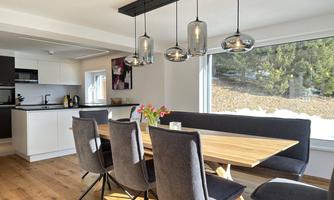A modern dining room with a large wooden table and comfortable chairs. Large windows let in plenty of light and offer a view of nature.
