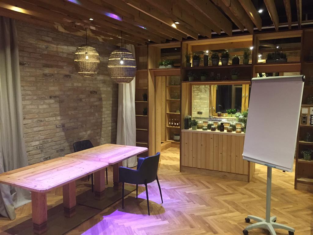 A modern meeting room with a long wooden table and a flip chart. The walls are made of stone and there is pleasant lighting as well as plants in the background.