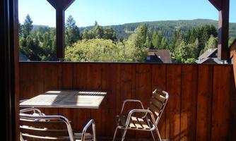 A cozy balcony with a table and two chairs. In the background, a picturesque forest landscape can be seen.