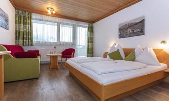 A cozy hotel room with a double bed and two armchairs. Large windows provide plenty of daylight and a comfortable atmosphere.