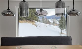 A modern dining area with a wooden table and elegant lamps. In the background, a snowy landscape and trees can be seen.