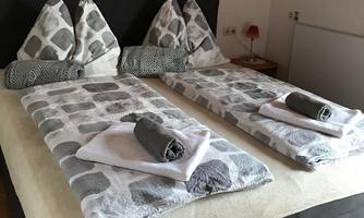 A cozy bedroom with two beds and decorative pillows. The bedding is light and the towels are neatly folded.