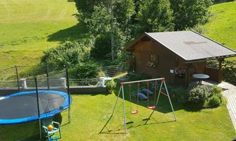 A beautiful garden with a trampoline, a swing, and a small wooden house. The surroundings are green and calm, perfect for children to play.