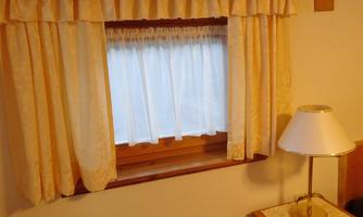 A simple window with light curtains. Next to the window, there is a lamp on a table.