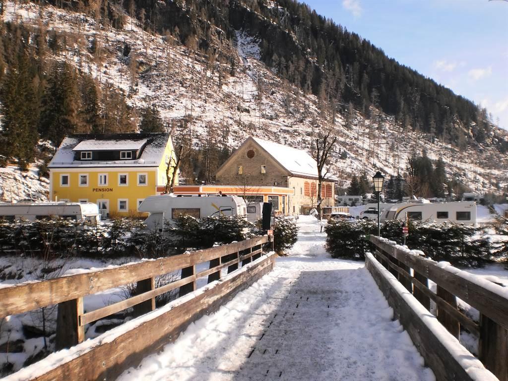 A winter village with snow-covered streets and mountains in the background. Colorful houses and caravans can be seen against a picturesque backdrop.