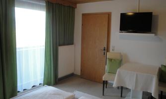 A simple room with two beds, a table, and chairs. Green curtains hang in front of the window, and a television is mounted on the wall.