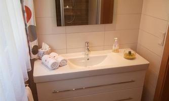 A modern bathroom with an elegant sink under a mirror. Fresh towels and a small decoration are on the shelf.