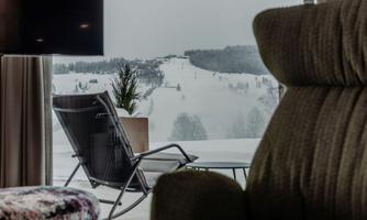 A cozy sitting area with a view of a winter landscape. Outside, snow lies on the ground and the mountains are visible in the distance.