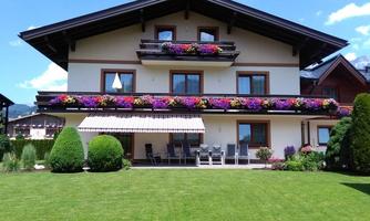 A beautiful house with blooming balconies and a well-kept garden. The terrace is equipped with cozy chairs.
