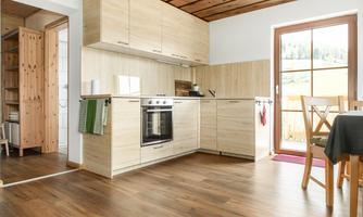 A modern kitchen with wooden shelves and a large window. The floor is made of wood and there is a table and chairs.