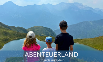 Three children are standing with a view of a picturesque landscape with mountains and two lakes. It is a beautiful day in nature.