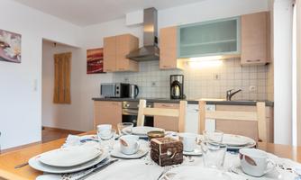 A modern kitchen with wooden cabinets and white tiles. The table is decorated and set with dishes and glasses for a cozy meal.