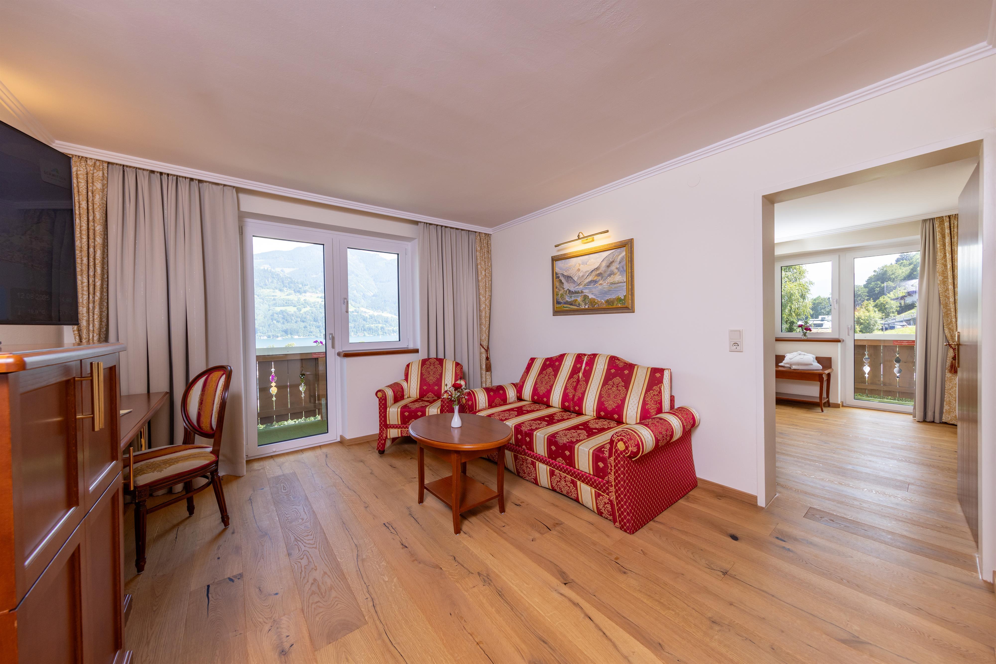 A cozy living room with a red sofa and wooden flooring. Large windows provide a view of the landscape.