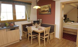 A cozy living kitchen with a dining table and chairs. The windows provide plenty of daylight in a modern atmosphere.