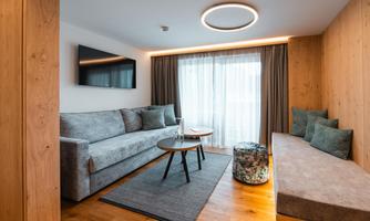 A modern living room with a gray sofa and wooden decor. Large windows let in plenty of light and create a friendly atmosphere.