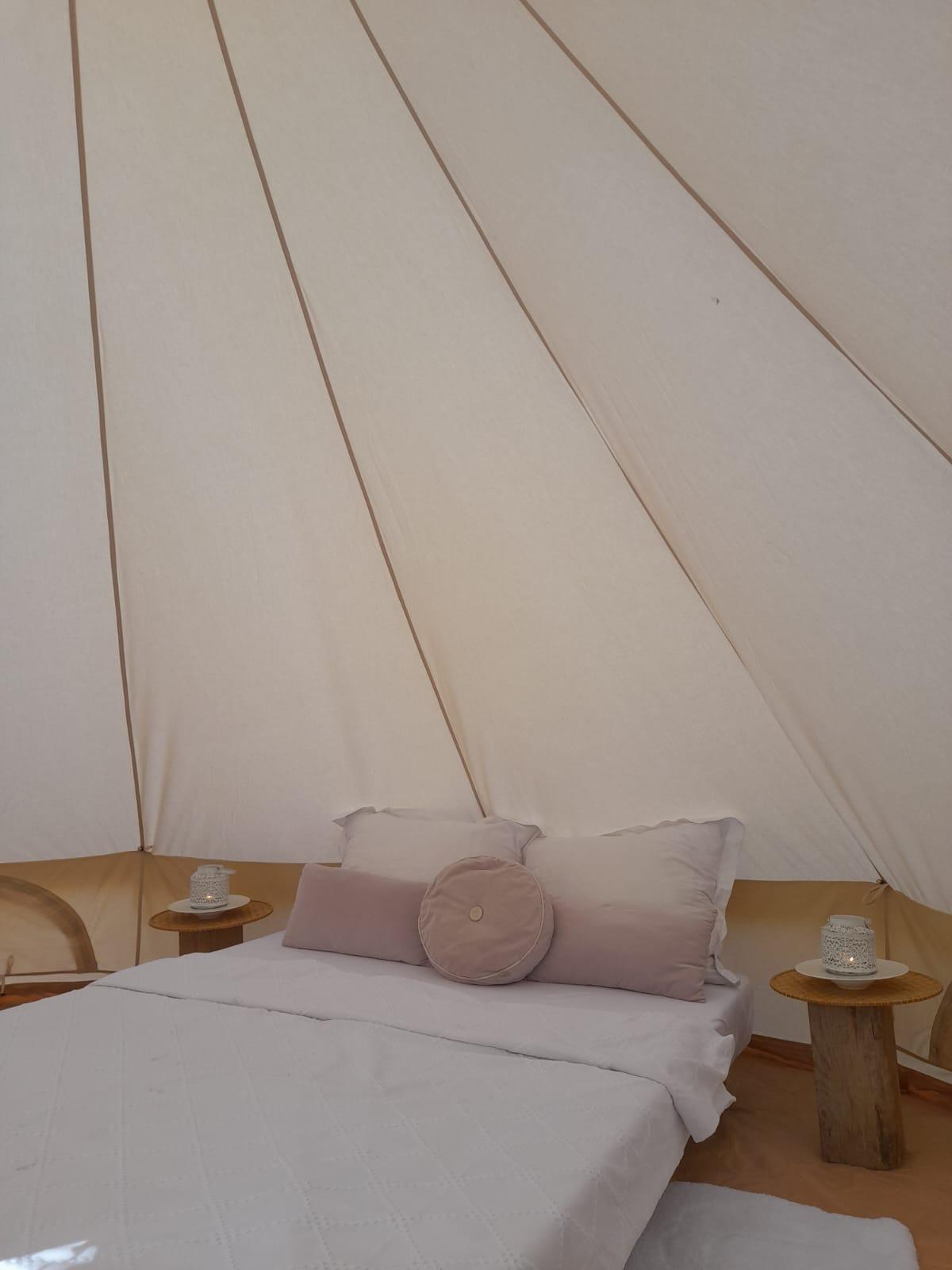 A cozy tent with a large bed and several pillows. Two small tables are next to the bed, on which cups are placed.