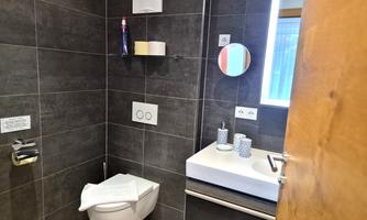 A modern bathroom with dark tiles. There is a sink, a toilet, and a large mirror.