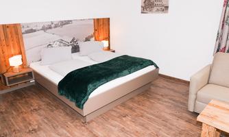 A modernly furnished bedroom with a large bed and a green throw. The wooden floor and the cozy seating area create an inviting atmosphere.